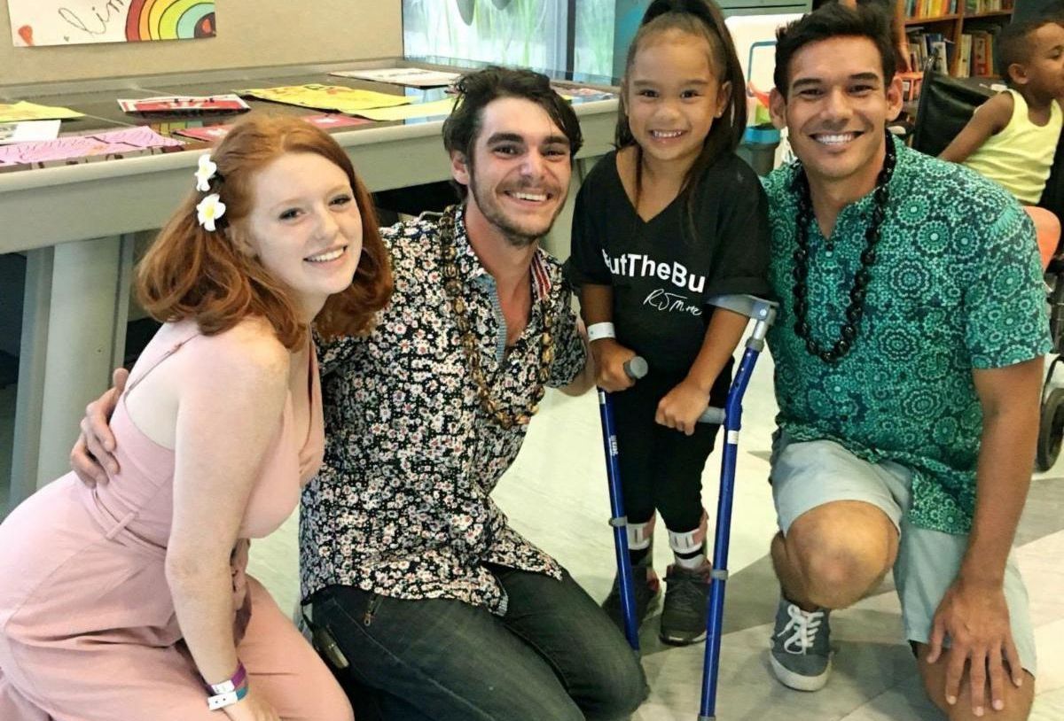 Young girl with canes surrounded by two men and a woman on their knees smiling