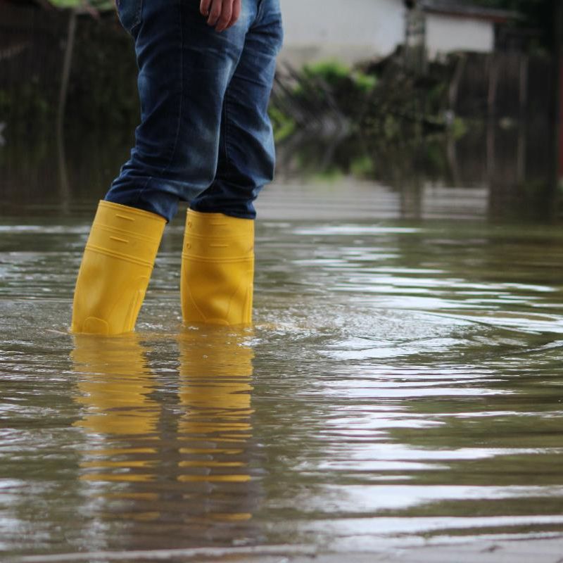 A view of someone's yellow rubber boots standing in a flooded street. 