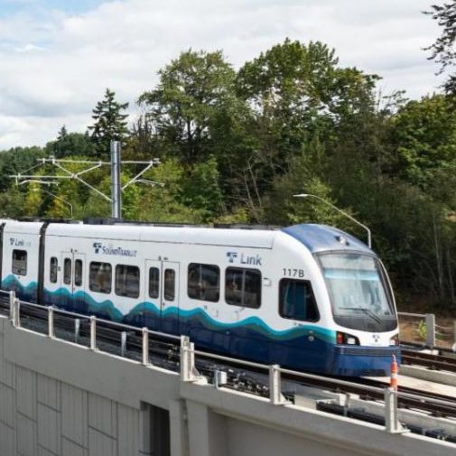 Two people smile at each other on a Link light rail platform with a train in the background.
