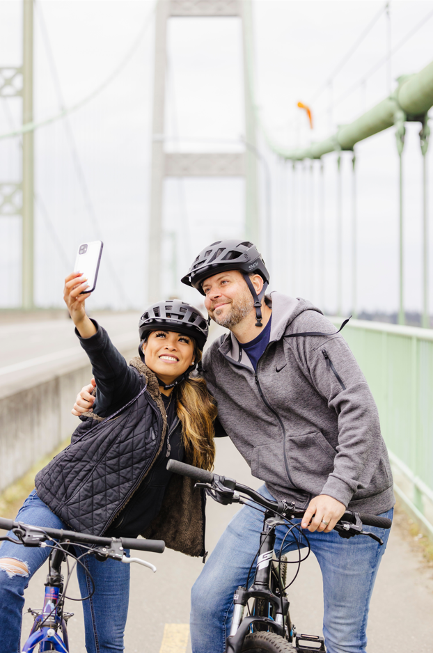 a female and male, both on bikes with helmets on stopped on the Narrows bridge to take a selfie. 