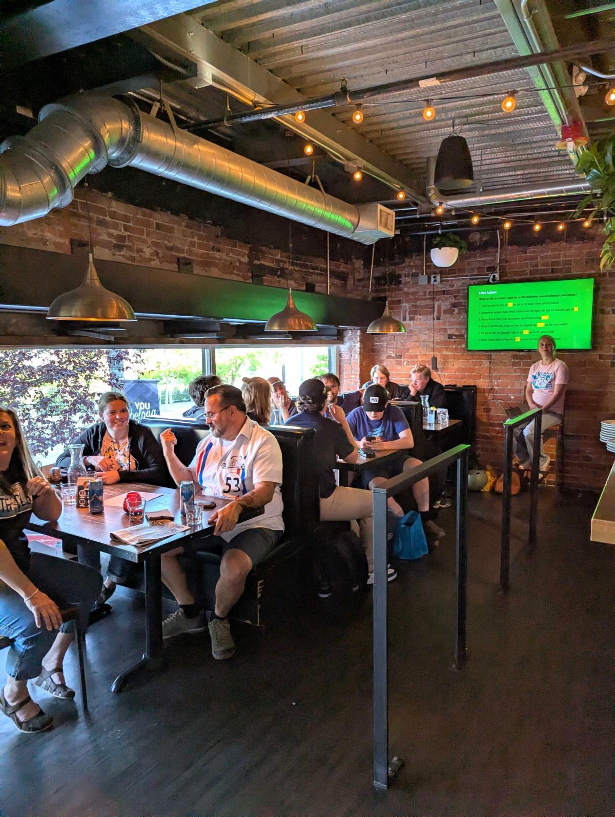 People in restaurant siting down playing trivia with screen in background