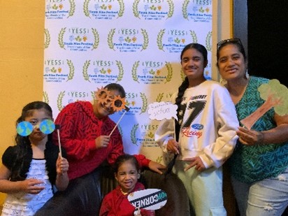 Family posing in front of a wall with the YESS film festival logos on it. 