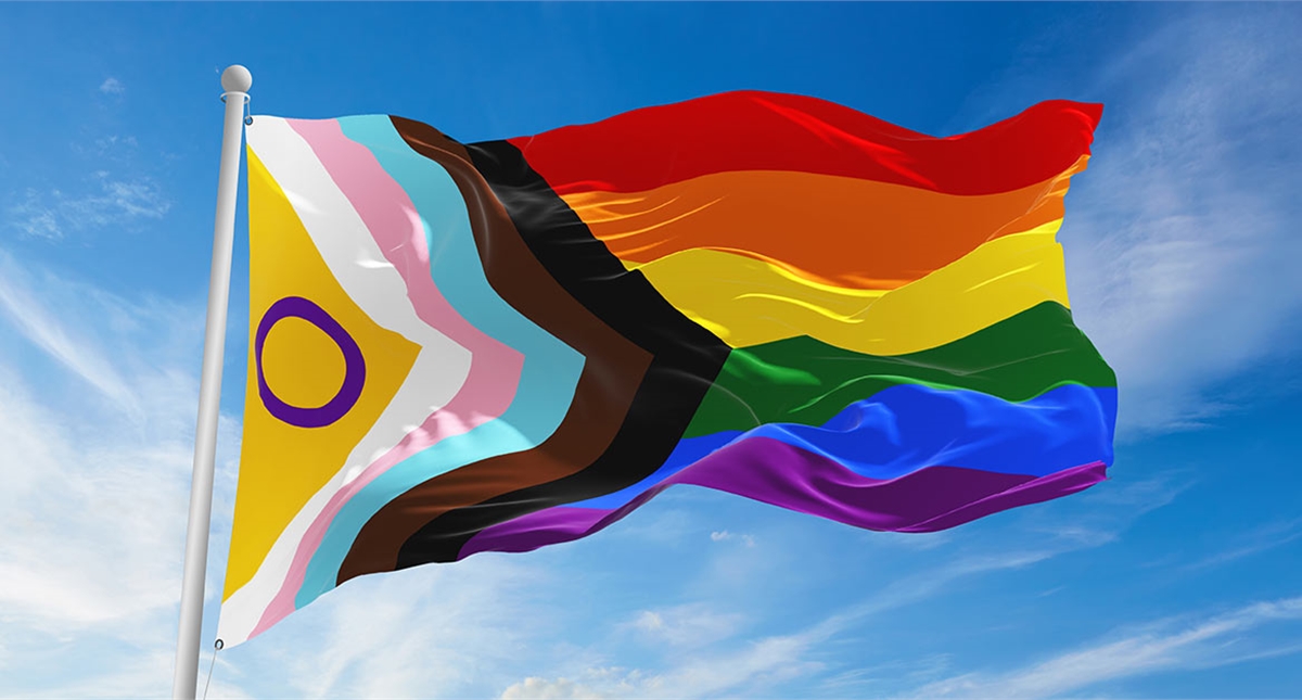 A progress pride flag against a blue sky