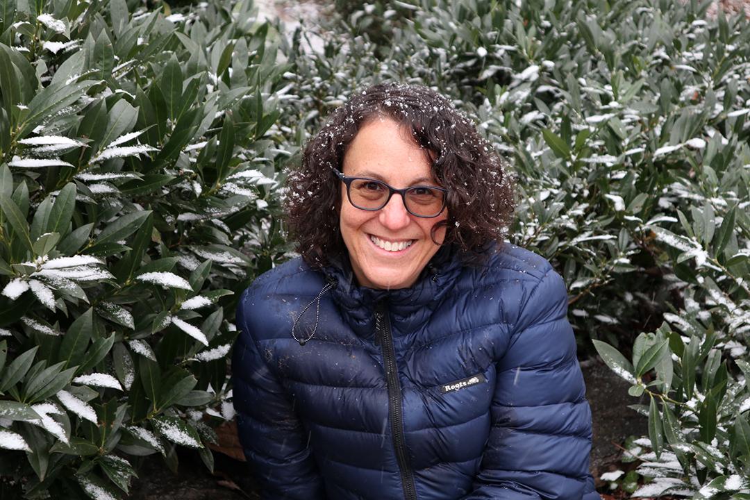 Melissa Feuer in the snow with green bushes wearing a coat