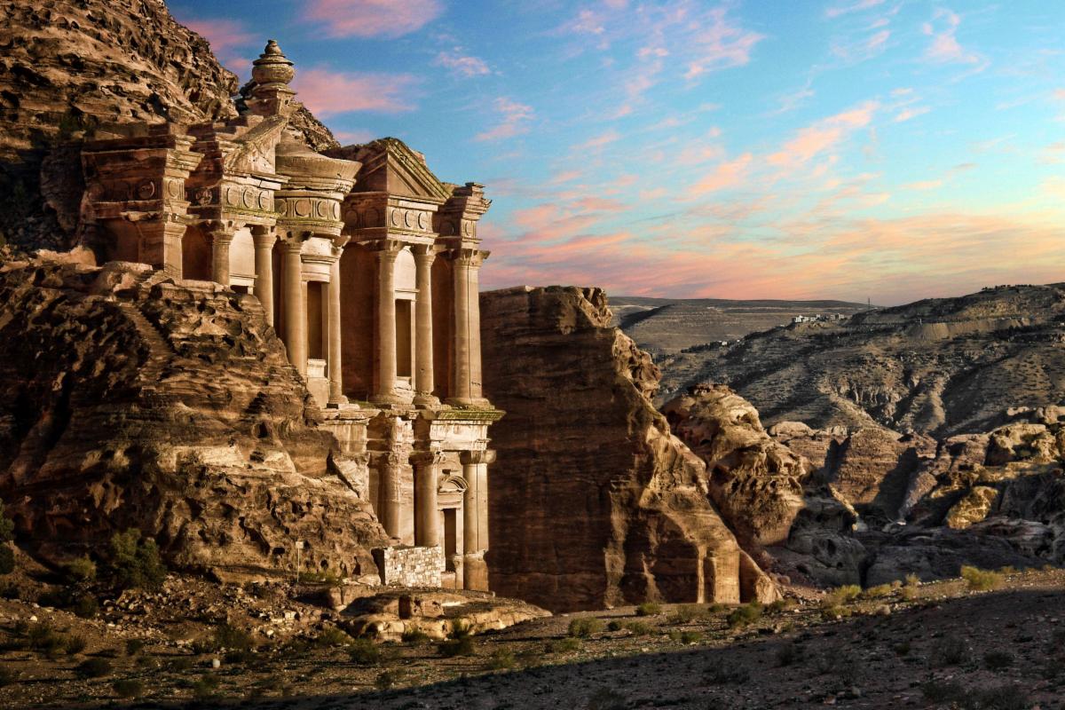 a building carved from stone in petra sits with mountains in the background