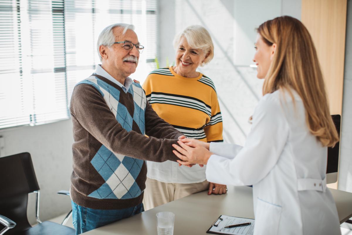 An older couple smiling and shaking hands with a doctor. 