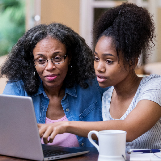 An older woman wearing glasses and reviewing information on a laptop at home with the help of her adult daughter. 