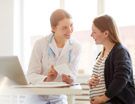 A doctor consulting with a pregnant woman in a clinical setting.