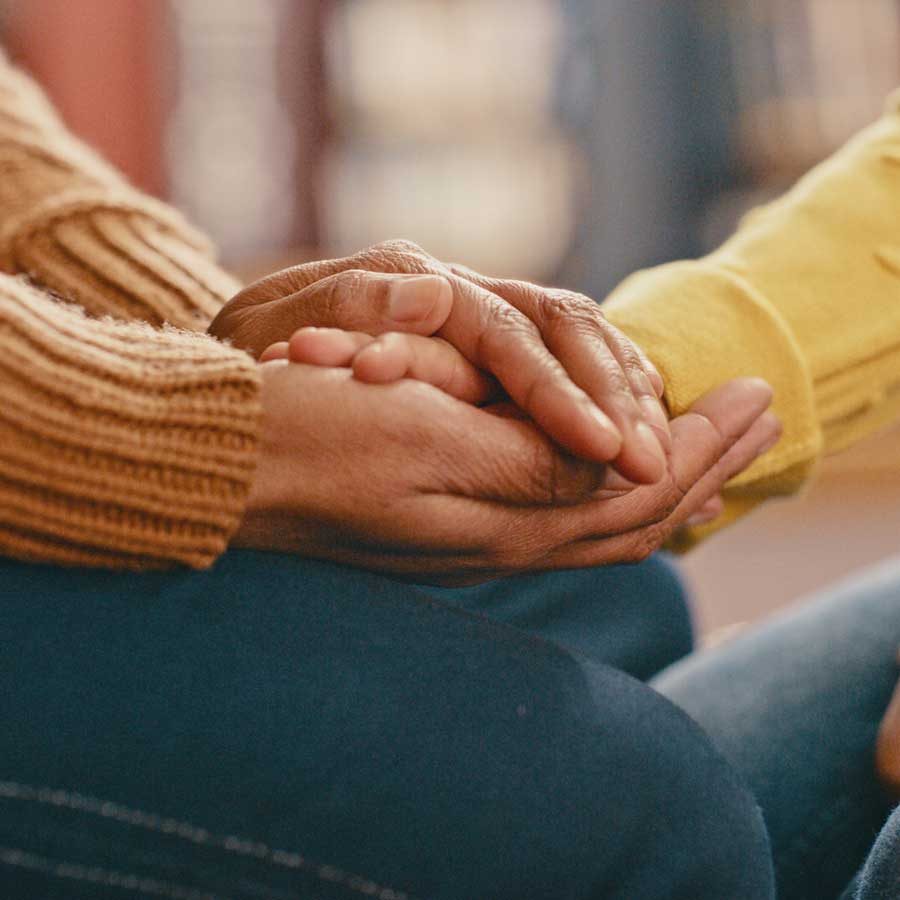 Close-up of a person clasping another person’s hand in both of their own in a kind, supportive way.   