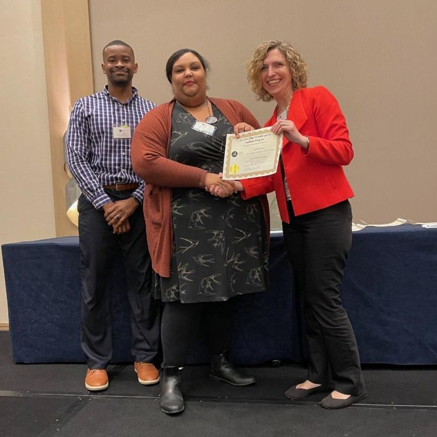 two women and a man pose with a certificate