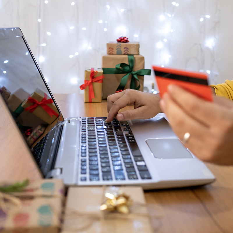 Hands typing on a keyboard and holding a credit card with gifts in the background