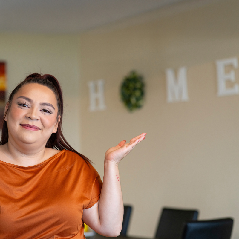 A person holding out their hand to show the word HOME on the wall behind them