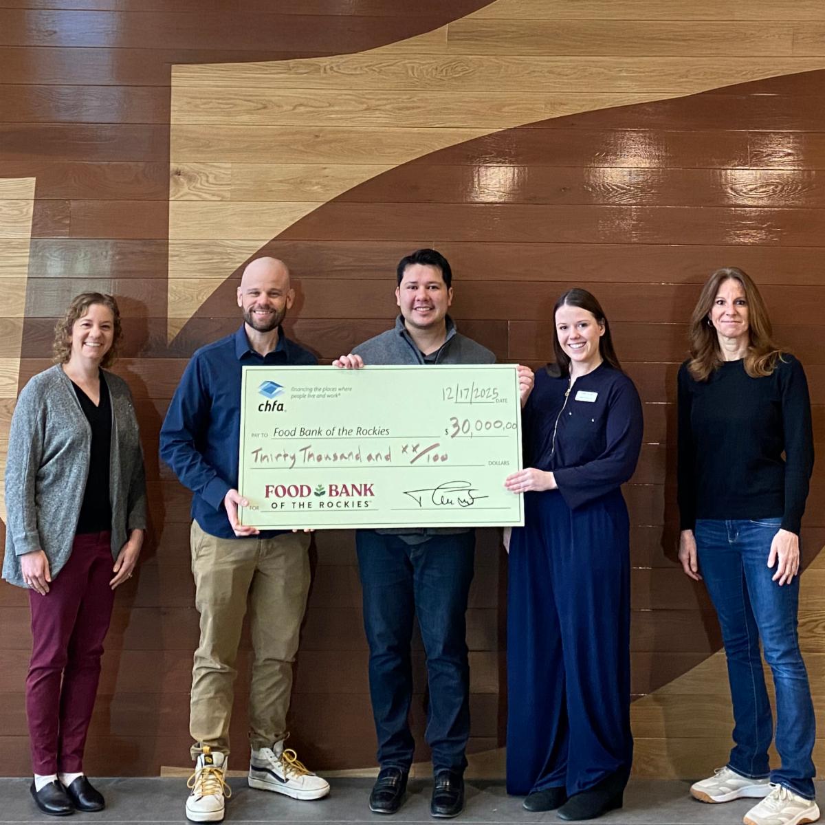 Five people standing in front of a wood wall holding a large check for Food Bank of the Rockies.