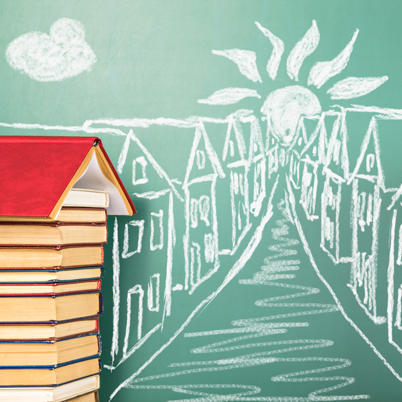 A stack of books on the side with a chalkboard in the back displaying a street and two rows of homes.