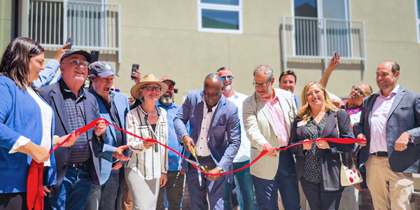 a large group of people holding a red ribbon while one person cuts it with giant scissors