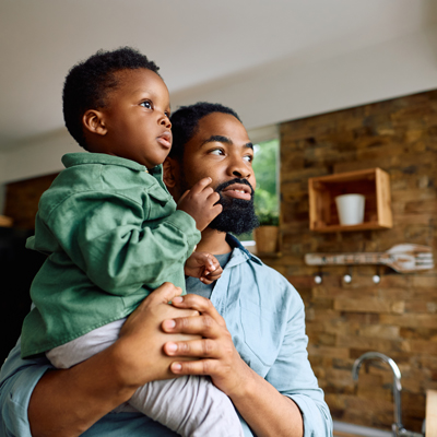 A person in a bricked room holding a child up to look outside
