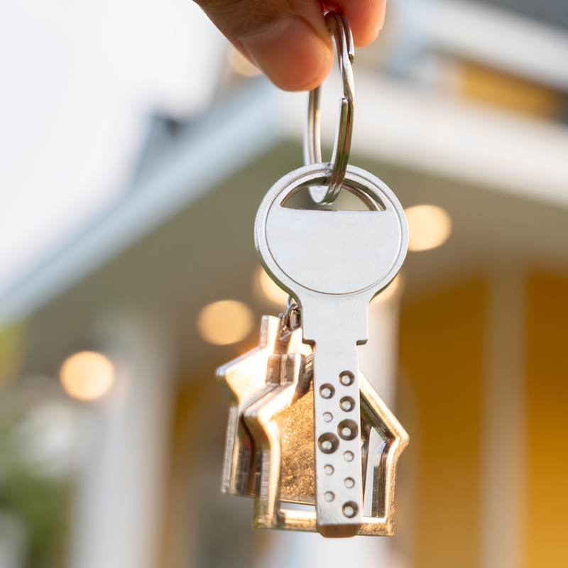 Fingers holding a key with a home in the background