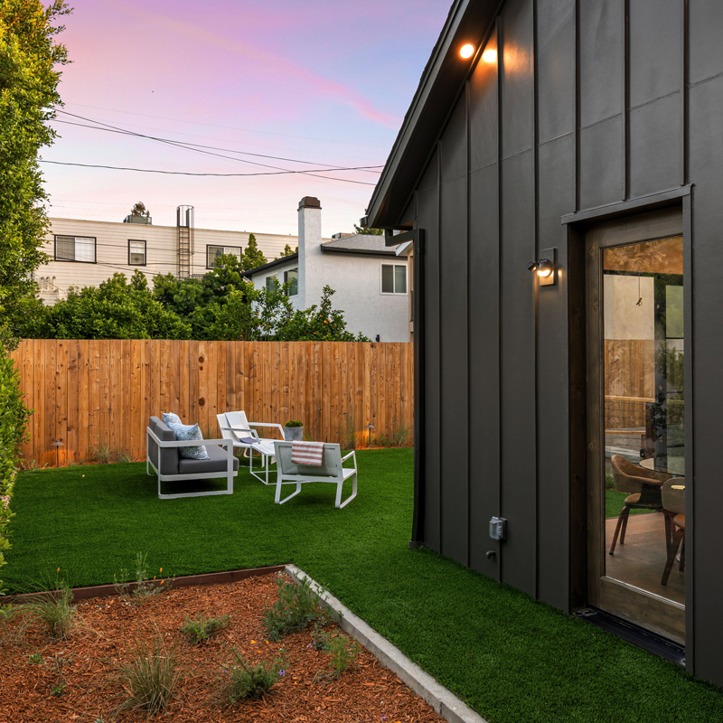 The side of an ADU in a backyard with a wood fence and pink sky.