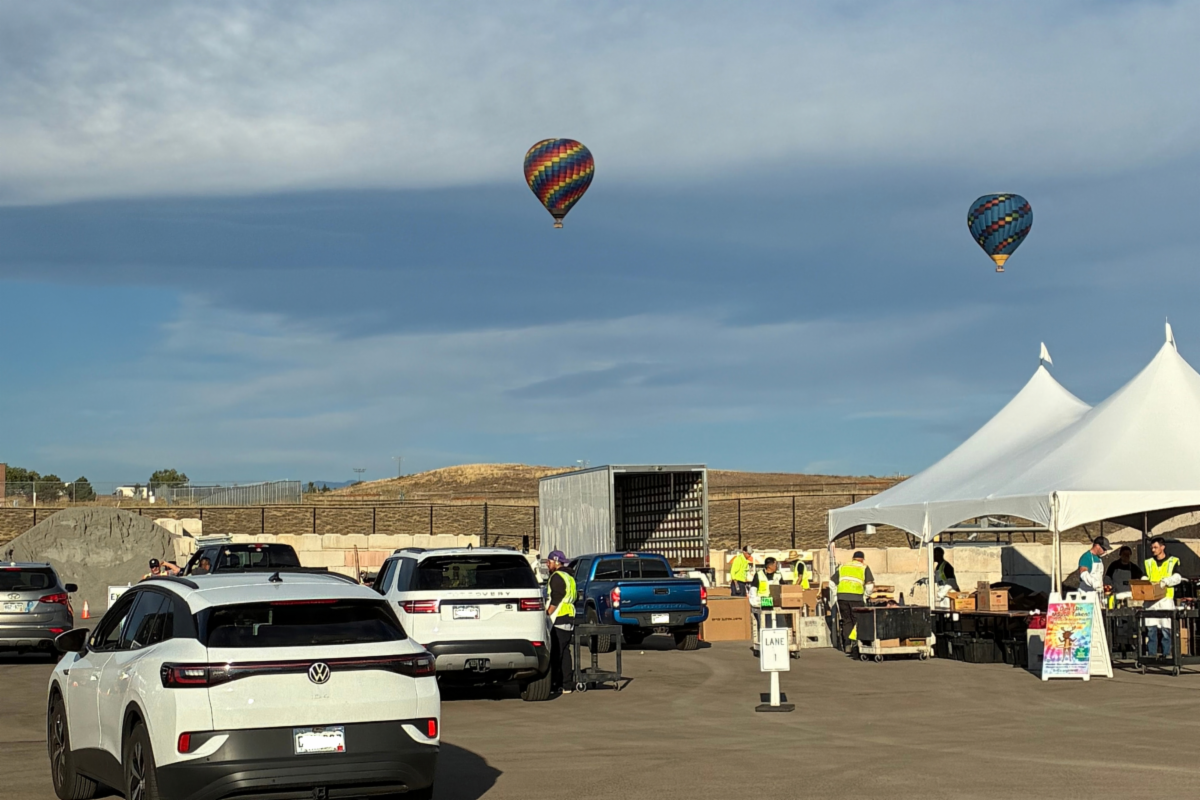Cars parked and tents set up in a parking lot at a community recycling event in Broomfield, Colorado.  Two hot air balloon float above the scene. 