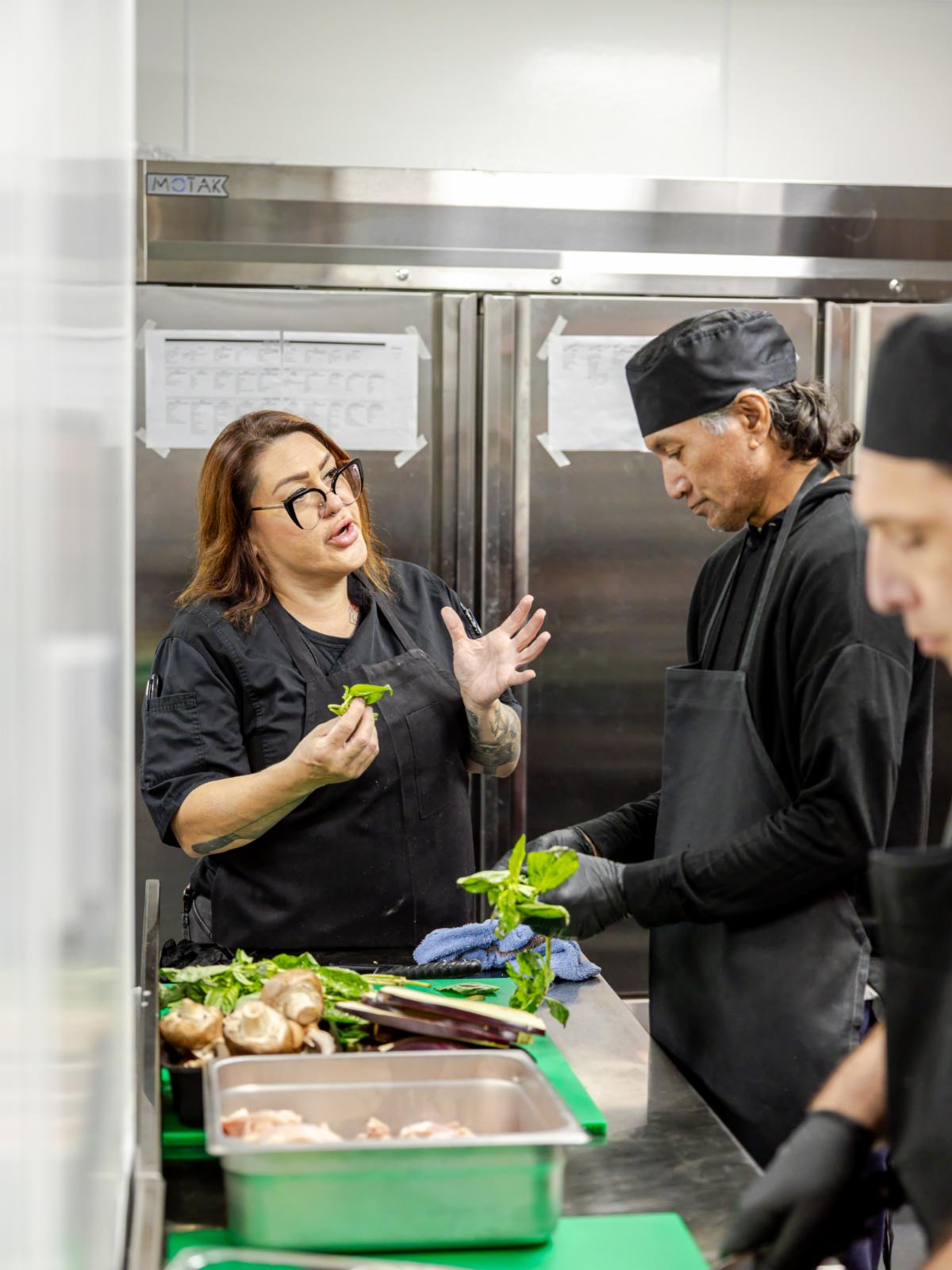 a woman in a food kitchen explaining preparation to two men
