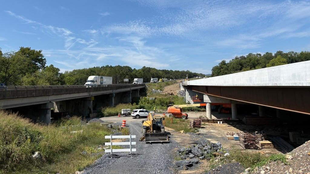Crews and construction equipment work on underside of bridge