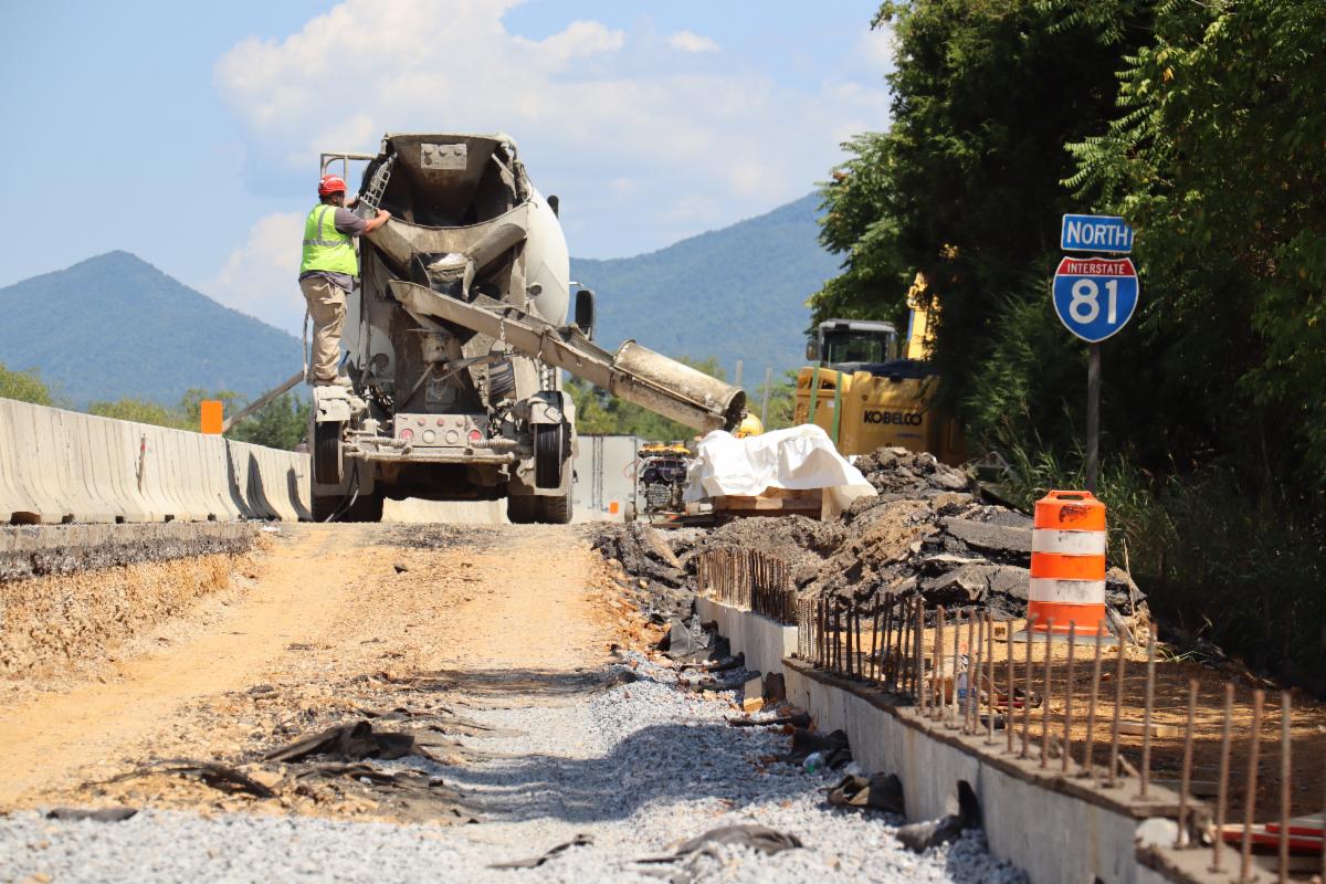 A cement truck and worker in a construction zone with an I-81 North sign visible