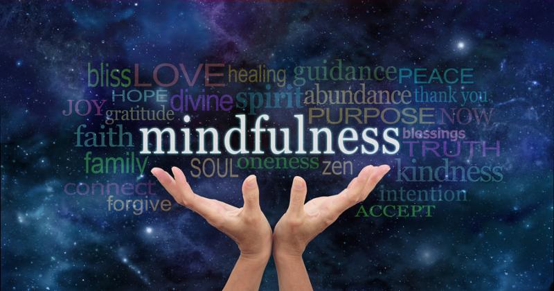 Female hands reaching up towards  the word  Mindfulness  floating above surrounded by a relevant word cloud on a dark blue night sky background