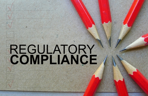 Word text Regulatory Compliance memo written on a brown craft paper as background with red pencils