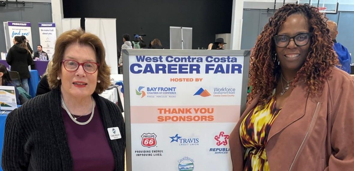Two women standing on each side of a sign that reads "West Contra Costa Career Fair"