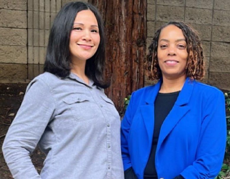 Two women standing side by side, with proud looks on their faces. 
