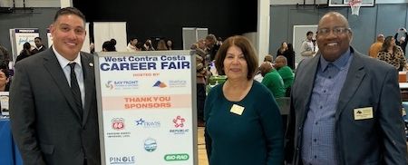 Two men, one woman standing on each side of a sign that reads "West Contra Costa Career Fair"