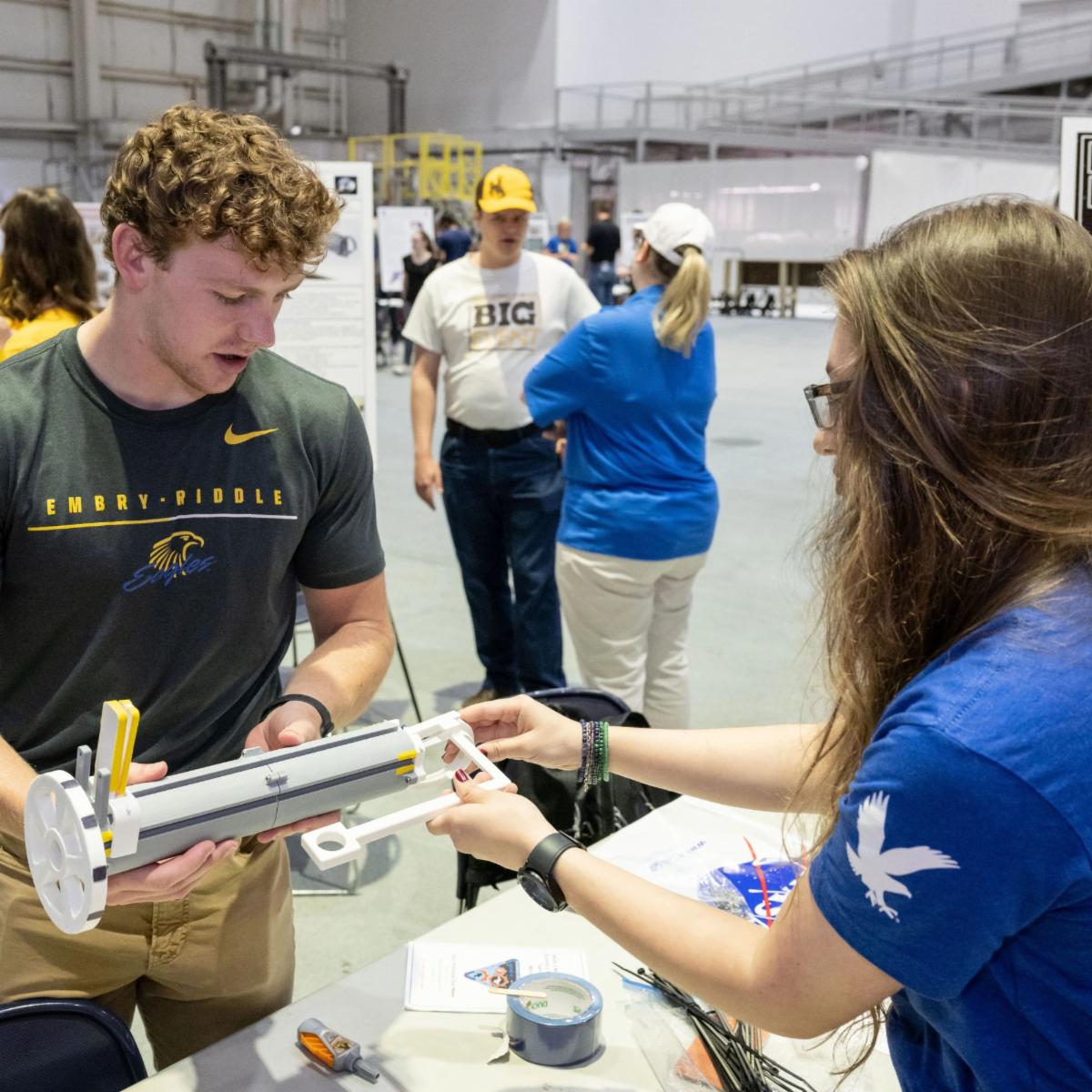 One male college student and one female college student work together on a white cylindrical piece of hardware