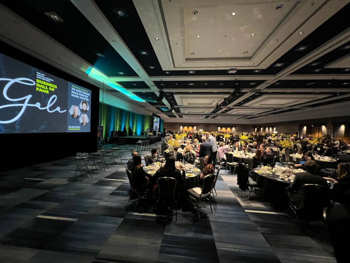 Guests of the JASWO Business Hall of Fame dinner seated at round tables eating and listening to a speaker on stage. 