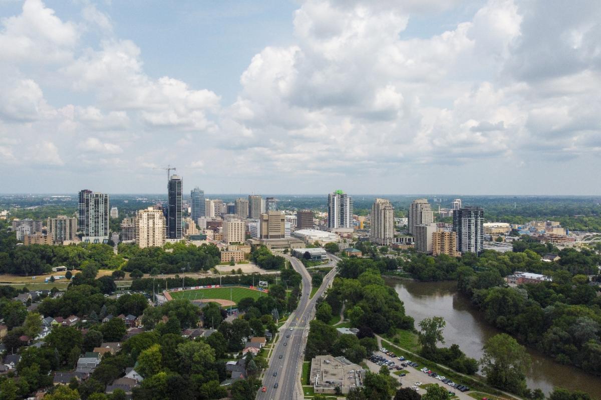 Aerial view of the London city skyline with tall buildings, a winding Thames river, and green parks under a partly cloudy sky.