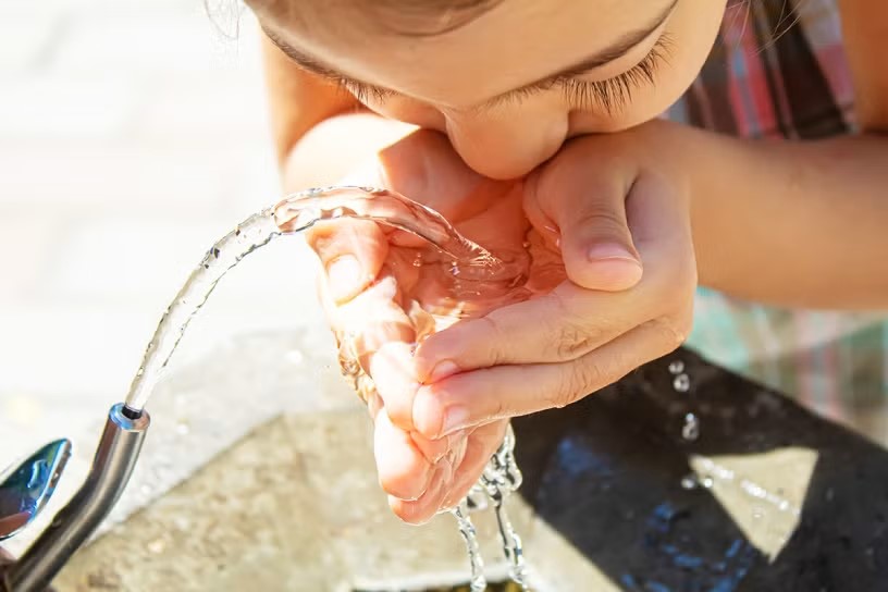 A child cups their hands to drink water from a water fountain
