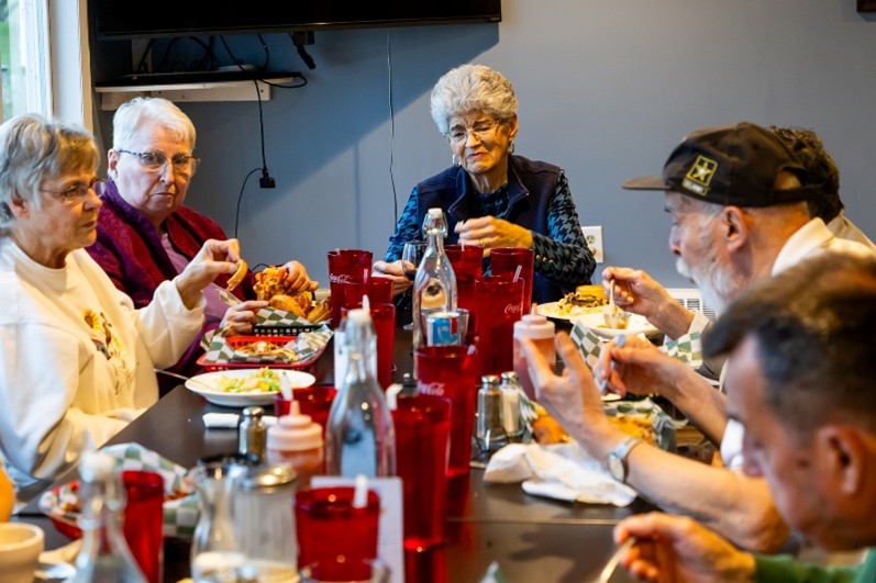 SAGe members and guests sit around a long table and eat dinner