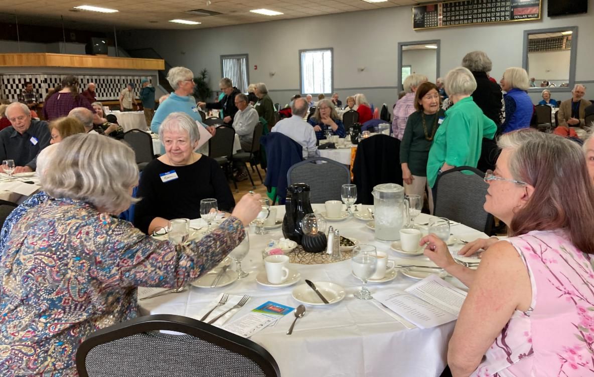 Members of the UMA Senior College sit at round tables to eat a buffet lunch.