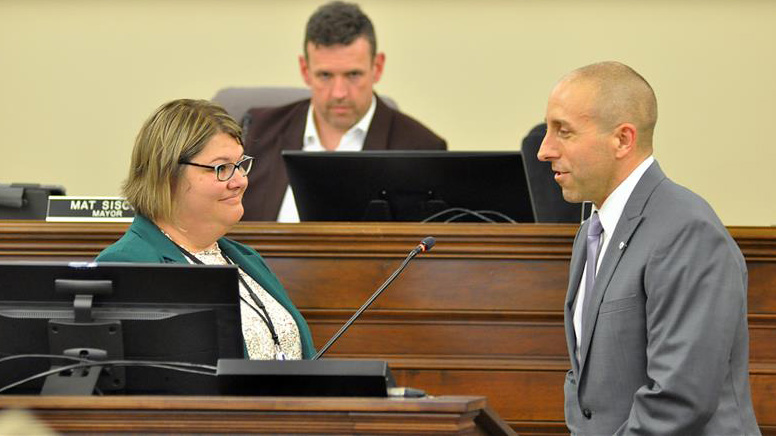 Marty Mako stands at the podium being sworn in as the City Clerk and mayor look on