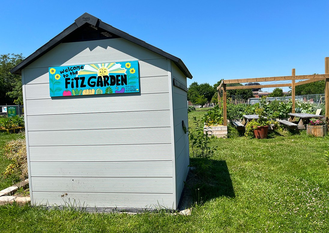 A storage shed with a sign that says, Fitz Garden, in front of the Fitz Community Gardens.