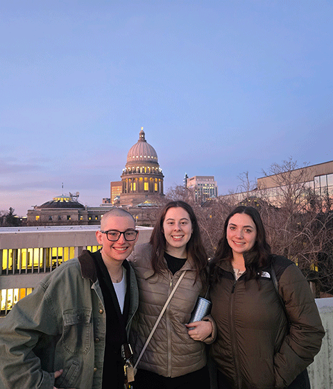 Three CDHD trainees posing and smiling at the camera at twilight with the Boise Capitol building lit up in the background