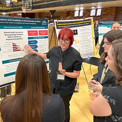 Corey is standing in front of a presentation board and talking to a group of students who are learning about mental heath at the university.