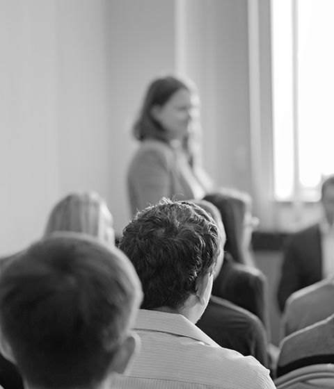 A group of men and women sitting in a conference listening to a speaker at the front of the room.