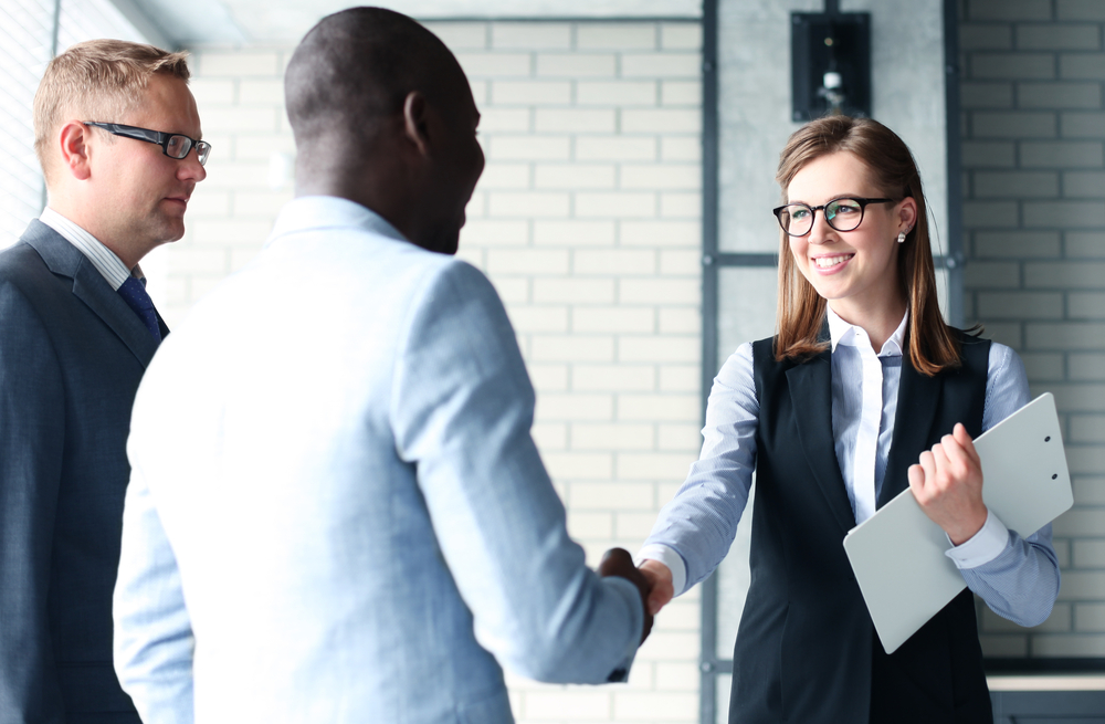 Woman shaking hands with a man while another man looks on.