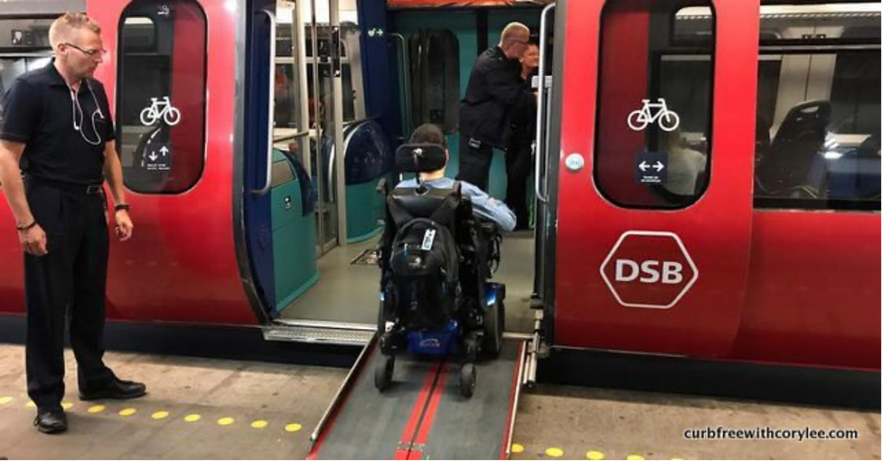 [Image: A man in a wheelchair independently boarding a red train, using an accessible ramp]. 