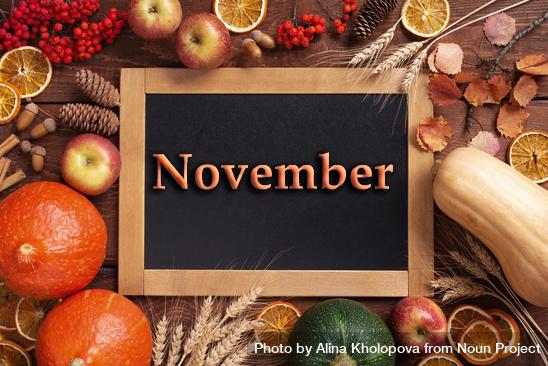 [Image: Squash, dried orange, apples and cinnamon sticks surrounding a board with the word November in orange and bold. Original photo by Alina Kholopova from The Noun Project (https://thenounproject.com)].