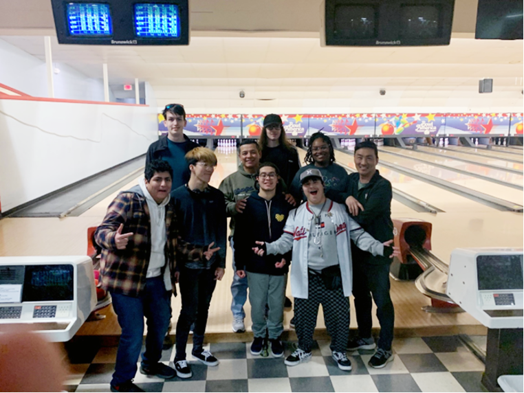 [Image: Kevina Brown (RAMP Coordinator), six mentees, and two parents are standing as a group in front of bowling lanes. Two of the six mentees have their arms outstretched and palms up at their sides. Everyone is facing the camera, except for one mentee who is facing to the right].