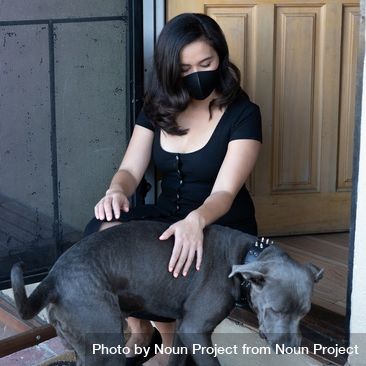 Woman sitting at doorstep with mask on petting her dog