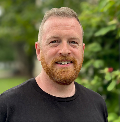 A headshot of a person wearing a black t-shirt