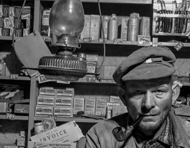 A black and white photograph of a general store owner in his shop in the 1940s