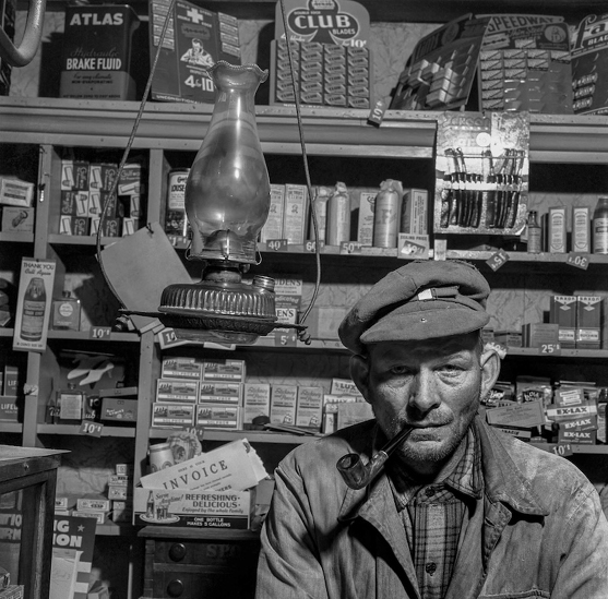 A black and white photograph of a general store owner in his shop in the 1940s